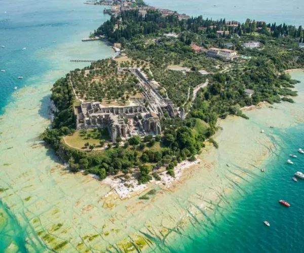 Aerial view of a lush island with ancient ruins, surrounded by turquoise water.