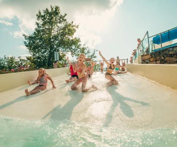 Children sliding down a water slide, smiling under a sunny sky.