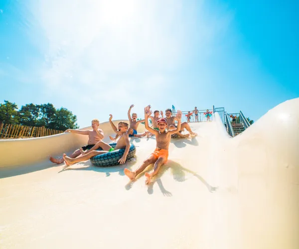 People sliding down a water slide, joyful expressions, sunny day.