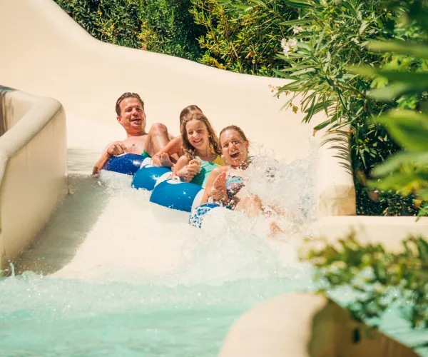 Family sliding down a water slide with joyful expressions and splashing water.