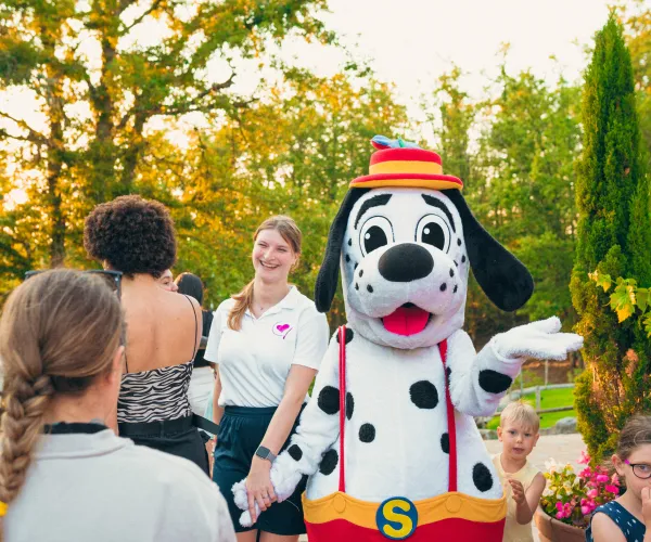 spotty with colorful hat greeting people outdoors.