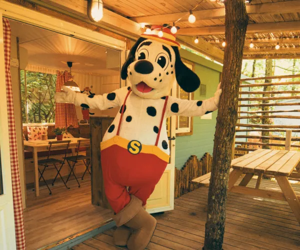 spotty in red shorts at a cozy wooden cabin entrance.