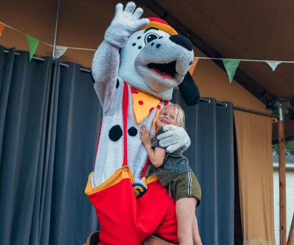 Boy hugging spotty on stage with colorful bunting overhead.