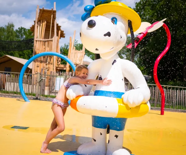 Child hugging large white dog statue at a water park.
