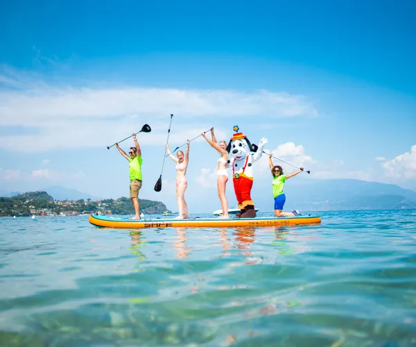 Four people in bright shirts paddleboarding on clear blue water under a cloudless sky.