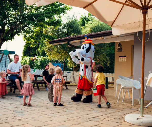 Kids smiling at a costumed character outside under a sunny patio.
