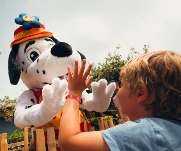 Child high-fives a cartoon dog character in costume outdoors.