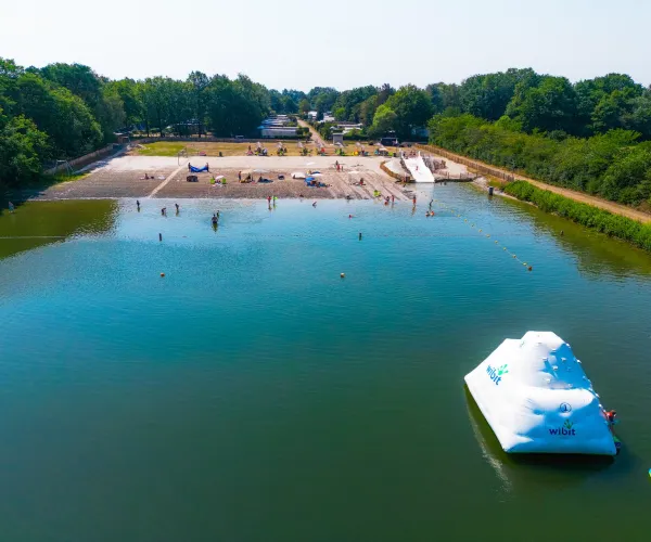 Calm lake scene with inflatable iceberg, beach, and trees under blue sky.