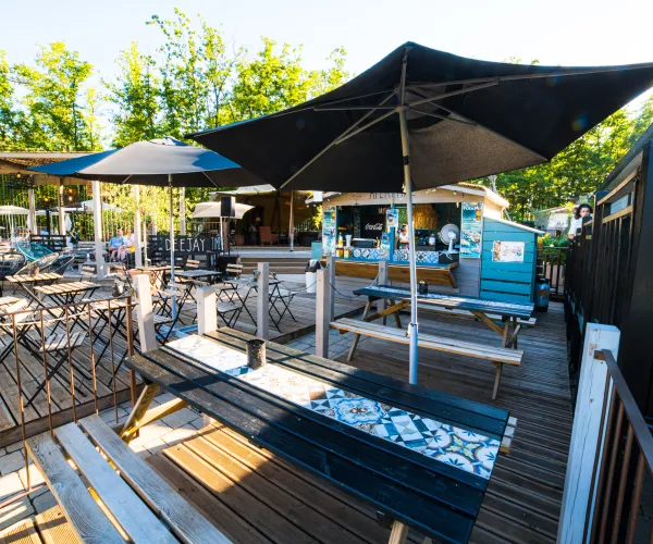 Outdoor patio seating with wooden tables under large black umbrellas.