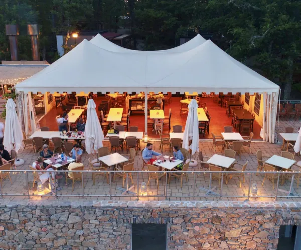 Outdoor restaurant with white canopy, tables, and chairs on a stone terrace at dusk.