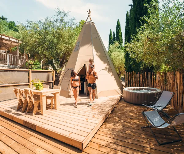 Couple exiting a tipi on a wooden deck with hot tub and chairs nearby.