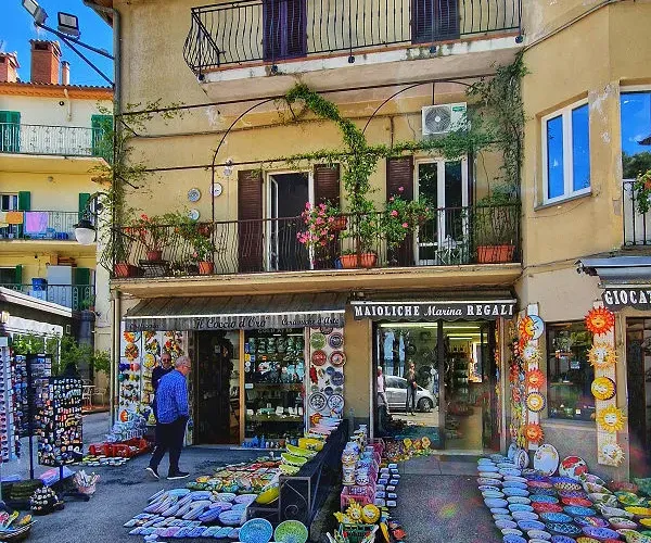 Colorful pottery displayed outside a shop in a sunny, rustic European street.