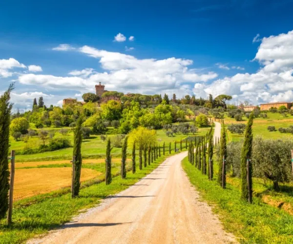 Tuscan countryside with a dirt road, cypress trees, and a scenic hilltop.
