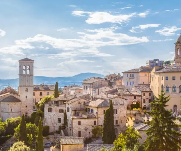 Historic townscape with stone buildings, hills, and a bright blue sky.