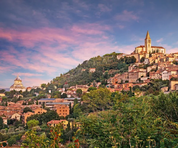Hilltop town with sunset sky, lush greenery, and rustic buildings.