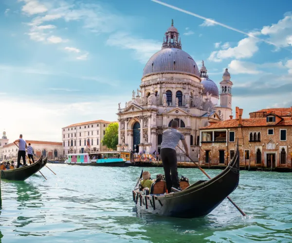 Gondolas on Venetian canal with a domed church under blue sky.