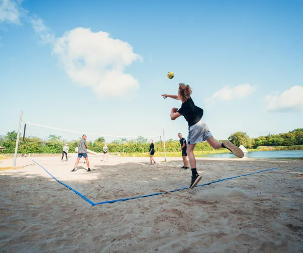 A person jumps to hit a volleyball on a sandy court under a clear blue sky.