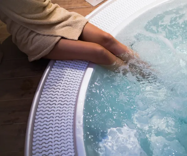 Woman in robe dipping legs into a bubbling hot tub.