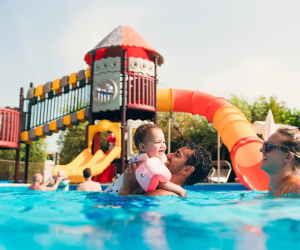 Family enjoying a pool with colorful water slides in the background.