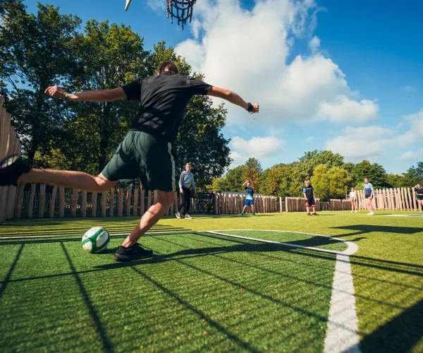 Man kicking soccer ball on outdoor field, blue sky above.