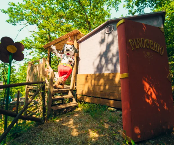 Pinocchio-themed playhouse with a large book facade and a clown figure, surrounded by trees.