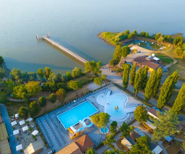 Aerial view of trasimeno lakeside resort with pool, pier, and trees.